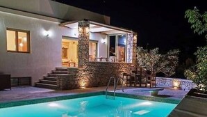 A swimming pool with a lounge chair, a stone wall, and a building with a staircase leading to an outdoor seating area. - Panorama Luxury Villa in Sitia, Crete (Sitia)