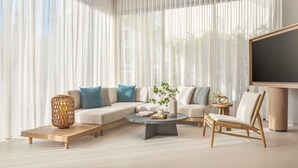 A modern living room with a sectional sofa, a coffee table, a side table, a floor lamp, and a large flat-screen TV. - The Amayen - Handwritten Collection (Binh Kien)