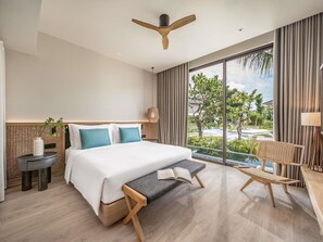 Une chambre d’hôtel moderne dotée d’un grand lit, d’un ventilateur de plafond, d’une vue sur l’extérieur et d’un coin salon avec une table et des chaises.