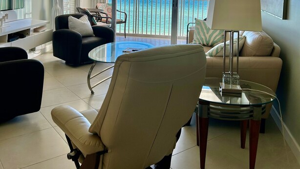 Een moderne hotelkamer met balkon en uitzicht op zee, een glazen bijzettafeltje, een bank en een stoel.