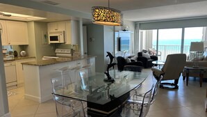 Een moderne keuken met witte kasten, een centraal eiland met barkrukken en een groot raam met uitzicht op de oceaan.