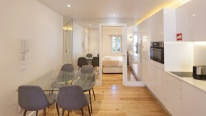 Une cuisine moderne avec des meubles blancs, un four encastré et un coin repas comprenant une table et des chaises en verre.