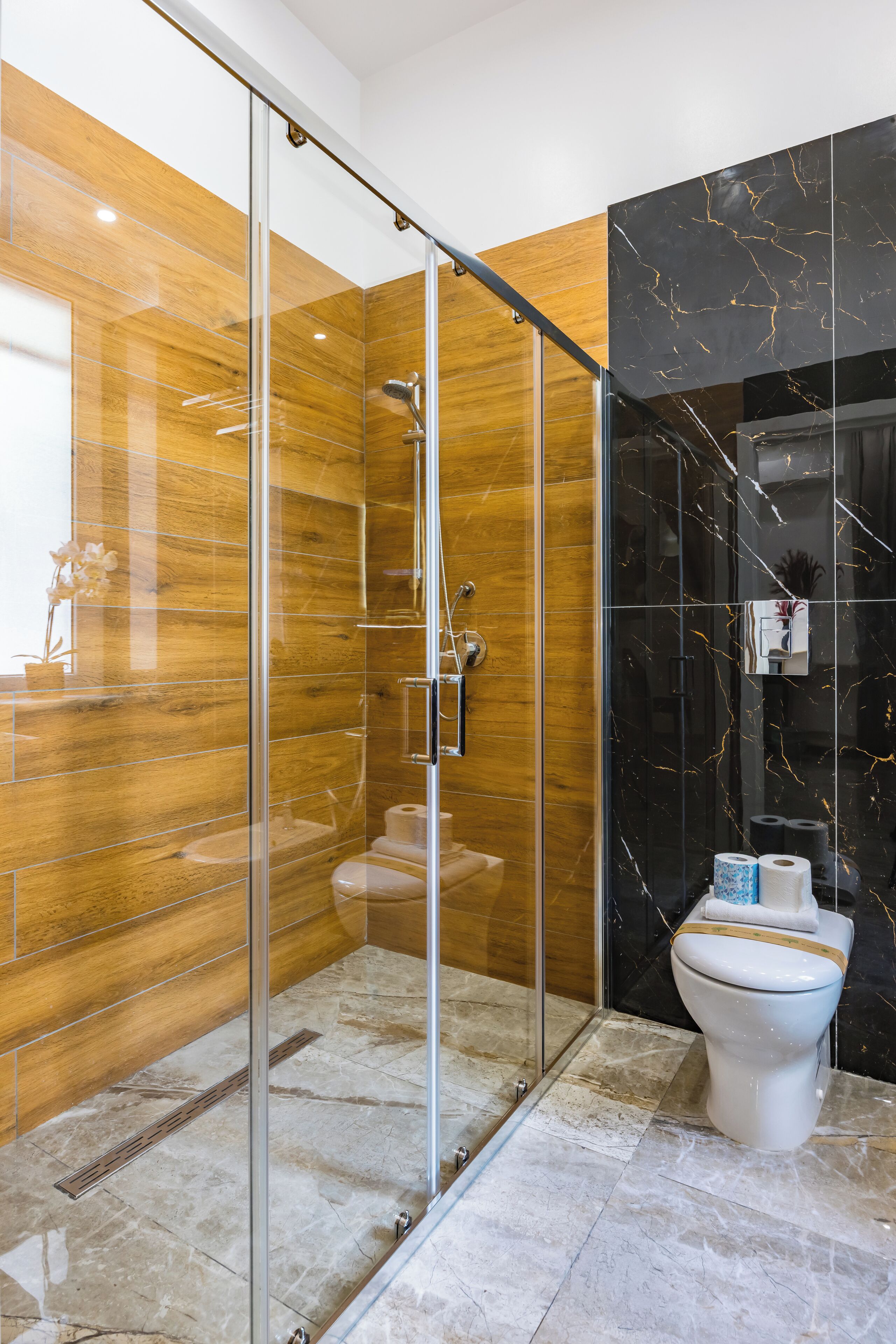 Um banheiro moderno com chuveiro em cabine de vidro, vaso sanitário e paredes de mármore.