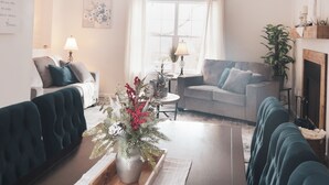 Una sala de estar con una mesa de centro de madera, dos sofás, una chimenea y un ventanal con cortinas.