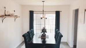 Comedor con mesa de madera oscura, sillas tapizadas, candelabro y ventana con cortinas.