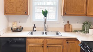 Una cocina con armarios de madera, un lavamanos de acero inoxidable, una ventana con vistas y una planta en la encimera.