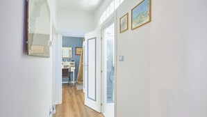 A hallway with wooden flooring, white walls, and framed pictures. There is a door leading to another room.