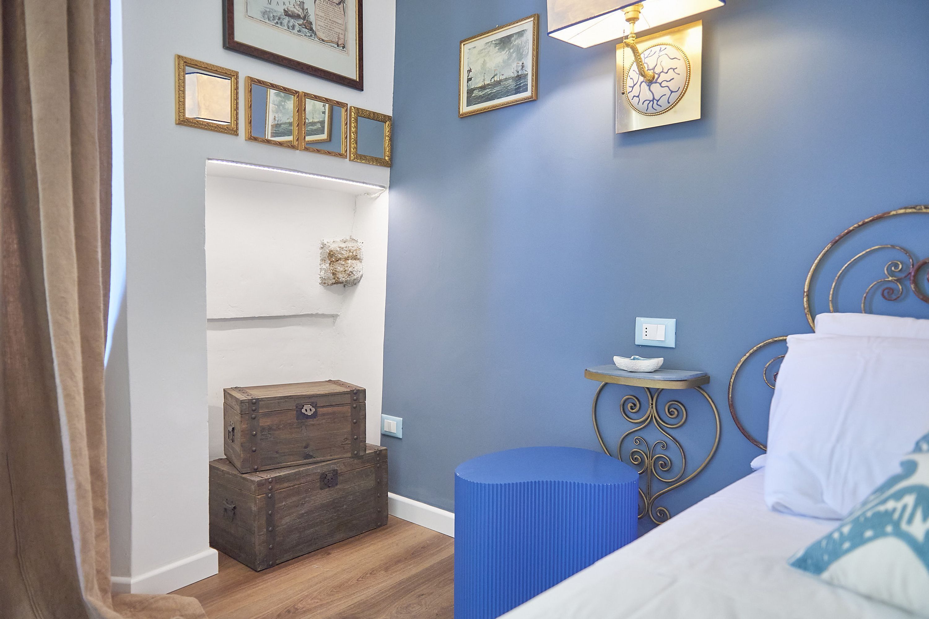 Un dormitorio con cama, mesita de noche, un taburete azul cilíndrico y cómodas de madera.