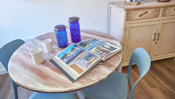 A wooden table with two blue glass jars, two white mugs, and an open magazine with travel photos.