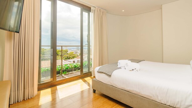 A hotel room with a large sliding glass door to a balcony, a bed with white linens, and a flat-screen TV mounted on the wall. - Cozy 2 Br apt in Candelaria (Bogotá)