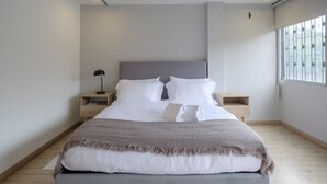 Ein modernes Schlafzimmer mit einem großen Bett, Nachttischen, einer Lampe und einem Fenster mit Jalousien.