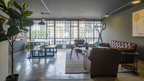 Ein modernes Wohnzimmer mit großem Fenster, einer Couch, einem Esstisch und einer Topfpflanze.