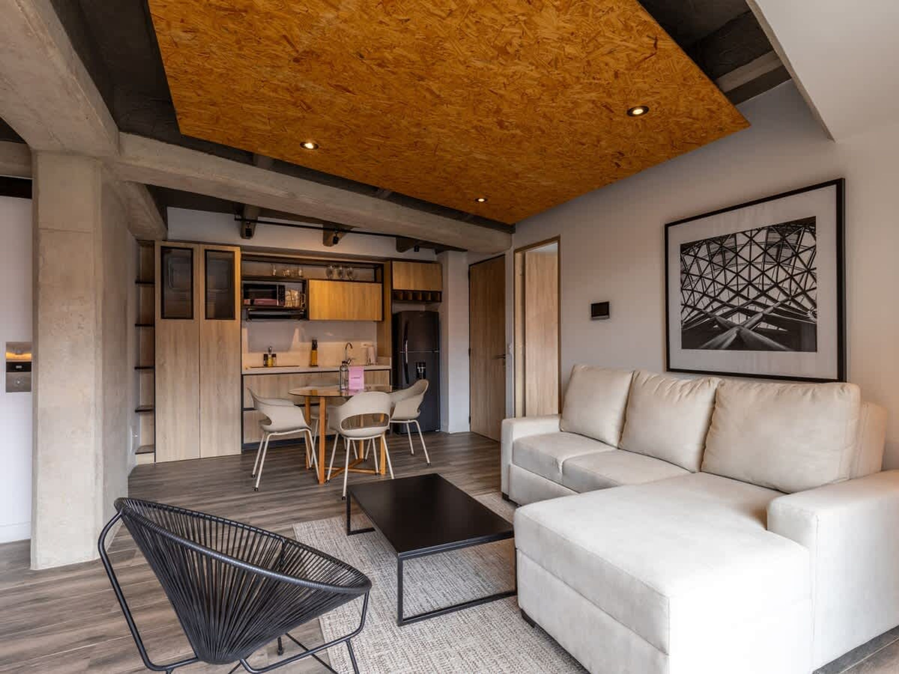 Een moderne woonkamer met een houten plafond, een witte bank, een zwarte salontafel en een eethoek met een houten tafel en stoelen.