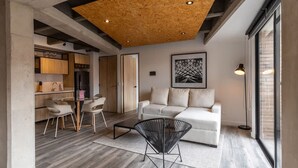 A modern living room with a wooden ceiling, a white sofa, a black chair, and a dining area with chairs and a table. - Stylish 1 BR in Chapinero (Bogotá)
