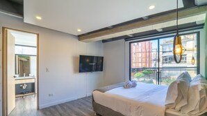 A modern hotel room with a large bed, a television mounted on the wall, and a window with a city view. - Stylish 1 BR in Chapinero (Bogotá)