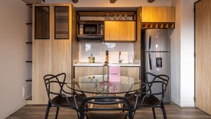 Eine moderne Küche mit einem Glastisch, schwarzen Stühlen, Holzschränken, einem Edelstahlkühlschrank und einer Mikrowelle.