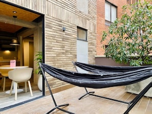 A modern outdoor seating area with a hammock, a dining table with chairs, and a potted plant.
