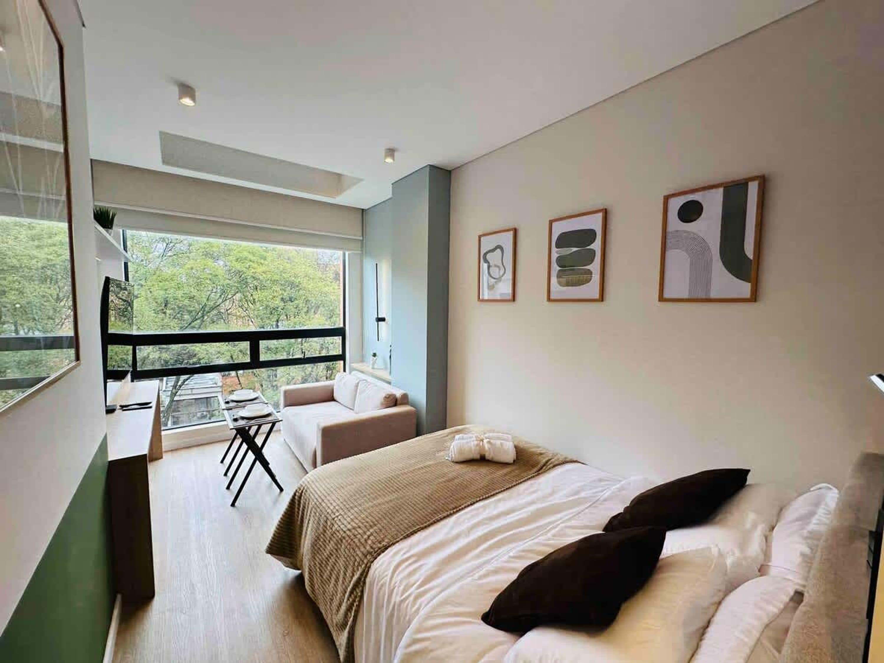 Et moderne hotelværelse med en stor seng, en balkon med bord og stole, samt kunst på væggene.