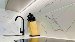 A modern kitchen with a sleek black faucet, a wooden utensil holder, and white marble tiles. - Amazing Apartment in Parque 93 (Bogotá)