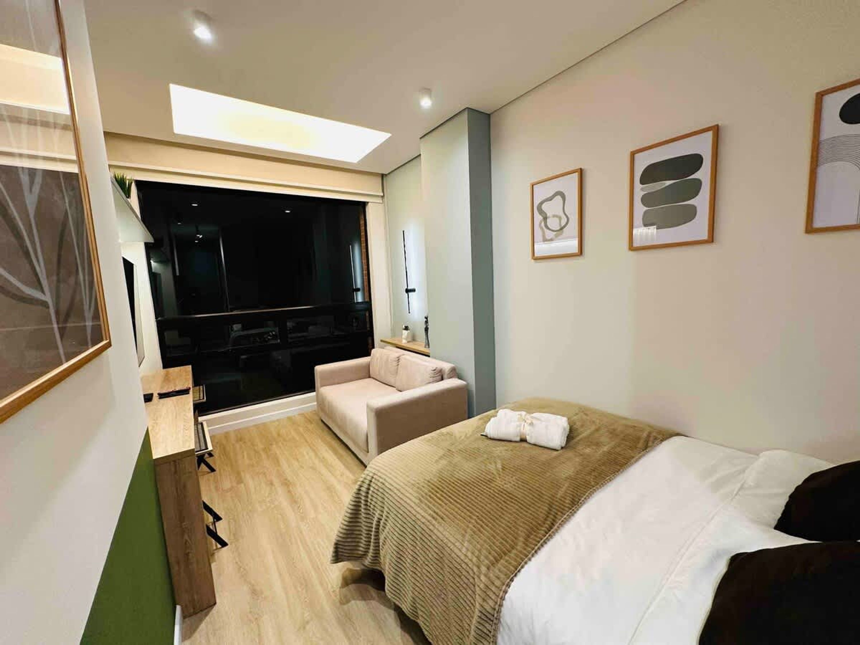 Habitación de hotel moderna con cama, sofá, escritorio y un ventanal grande.