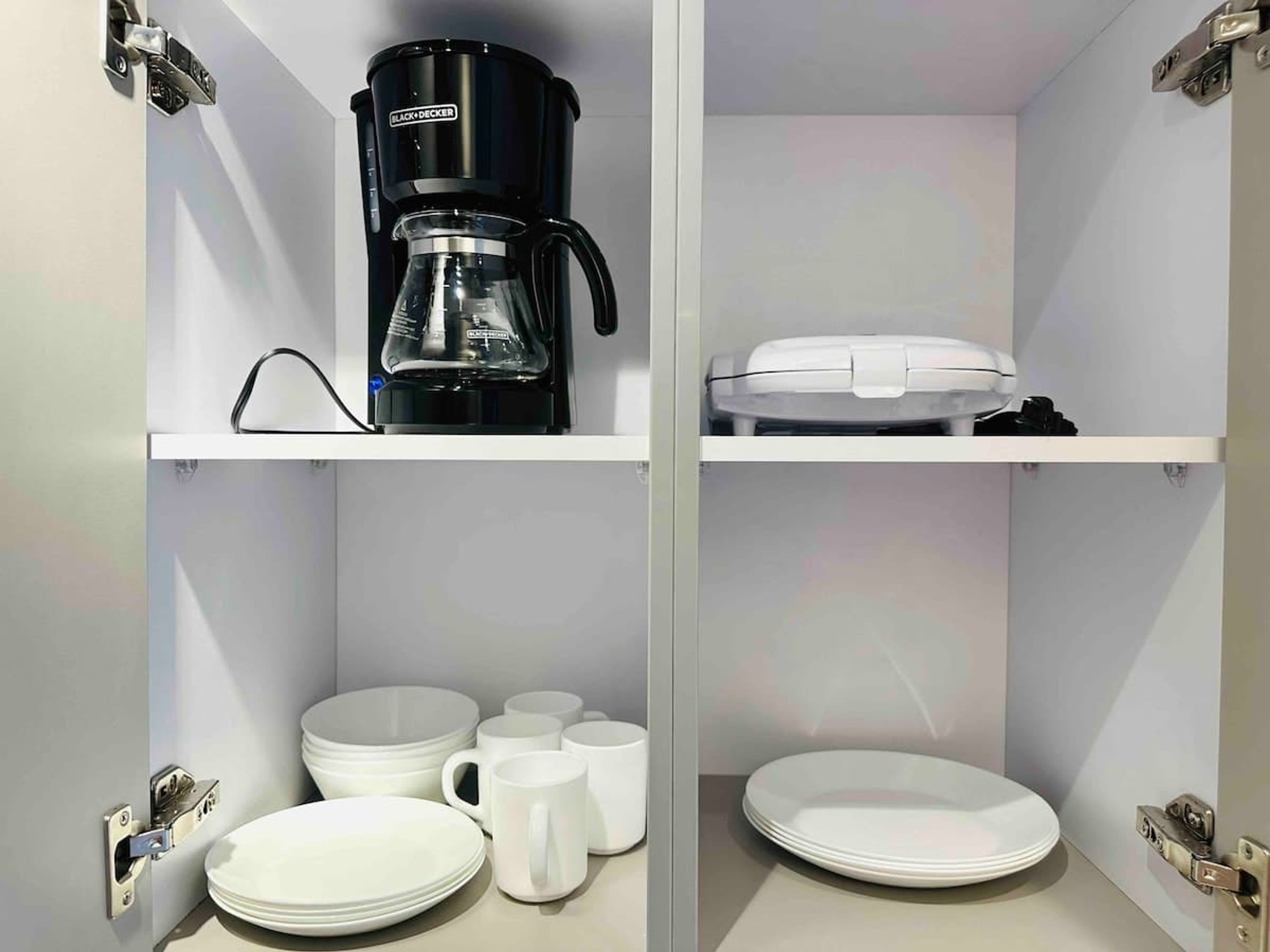 A compact kitchen with a coffee maker, a toaster, and a microwave on the upper shelf, and a sink with a mirror below.