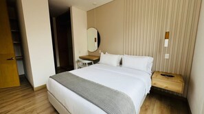 A hotel room with a large bed, a bedside table, a chair, a mirror, and a wardrobe.