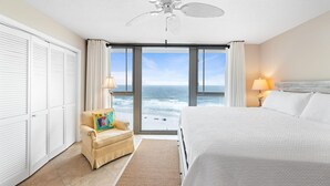 A hotel room with a bed, a chair, a ceiling fan, and a view of the ocean. - Perdido Towers West 1005 (Pensacola)