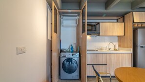 A compact kitchen with a built-in washing machine, wooden cabinets, and a small dining area with a table and chairs. - Modern 1 BR in Chapinero (Bogotá)