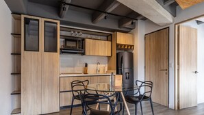 A modern kitchen with wooden cabinets, a black refrigerator, and a glass dining table with chairs. - Stunning 1 BR in Chapinero (Bogotá)