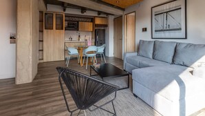 A modern living room with a grey sofa, a black chair, and a coffee table. There is a kitchen area with wooden cabinets and a dining table with chairs. - Classy 1 BR in Chapinero (Bogotá)