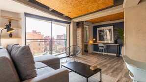 A modern living room with a sofa, a coffee table, and a dining area with chairs. There is a large window providing a view of buildings outside. - Classy 1 BR in Chapinero (Bogotá)