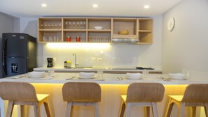 Uma cozinha moderna com ilha central, banquetas de madeira e prateleiras embutidas com copos e utensílios de cozinha.