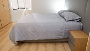 Uma cama de solteiro com cabeceira cinza e mesa de cabeceira de madeira ao lado.