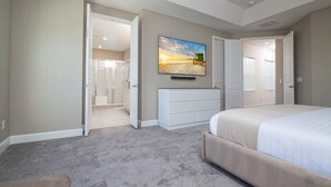 Un dormitorio con una cama grande, un aparador, un cuadro y una puerta abierta que da al baño.