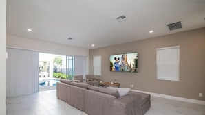 Un salón amplio con un sofá seccional grande, un televisor de pantalla plana montado en la pared y un ventanal corredero que da a un espacio exterior.