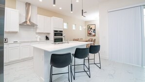 Una cocina moderna con armarios blancos, una isla central con taburetes y luces colgantes.