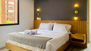 Ein modernes Hotelzimmer mit einem großen Bett, zwei Nachttischen, einem Fenster mit Blick auf ein Backsteingebäude.