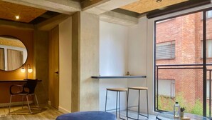 Ein modernes Zimmer mit einem großen Fenster, einem runden Spiegel, einem blauen Hocker, zwei Barhocker und einem kleinen runden Tisch.