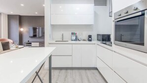 Une cuisine moderne avec des meubles blancs, un four encastré et un plan de travail sur lequel se trouve une machine à café.