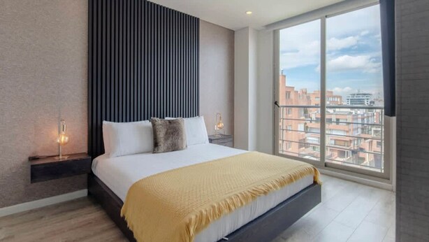 Une chambre moderne dotée d’un grand lit, offrant une vue sur la ville, et présentant un décor mural original.