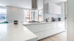 A modern kitchen with white cabinetry, a central island, a stainless steel range hood, and a view of the outside through large windows. - Modern 3BR in Usaqu n (Bogotá)
