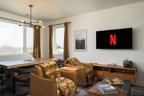 A modern hotel room with a large TV, a dining area, and a cozy seating area.