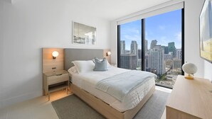 Un dormitorio moderno con una cama grande, mesitas de noche, un escritorio y vistas a la ciudad.