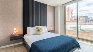 Et moderne hotelværelse med en stor seng, to sengeborde med lamper, udsigt til byen gennem store vinduer og en væg med struktur.