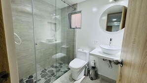 Moderni kylpyhuone, jossa on lasiseinällä varustettu suihku, wc, peilillä varustettu pesuallas ja roskakori.