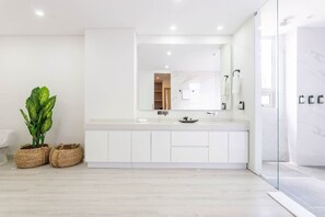 Un baño moderno con un tocador blanco, un espejo grande y una cabina de ducha de vidrio.