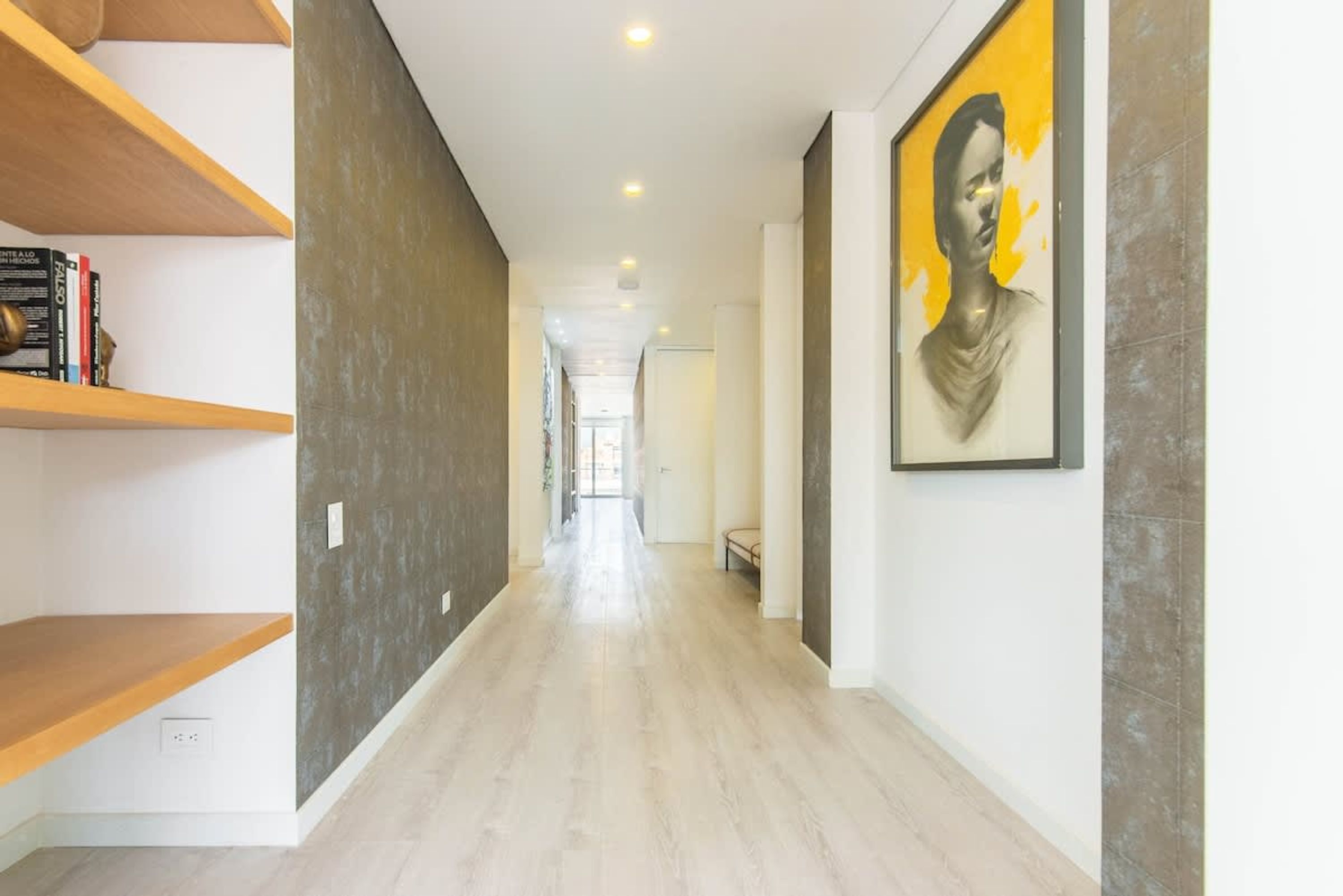A hallway with a wooden shelf, a framed portrait, and a light-colored floor.