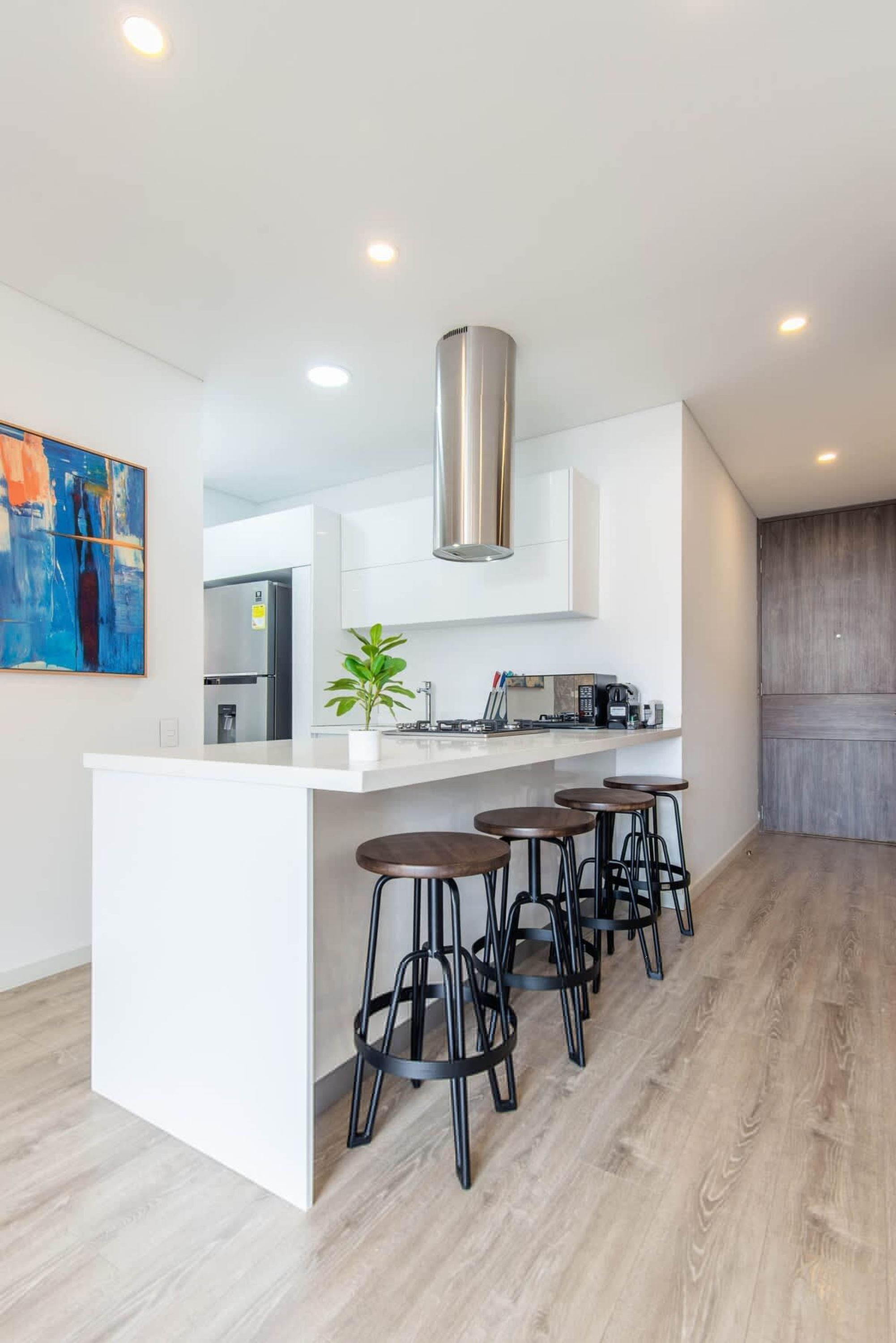 Una cocina moderna con armarios blancos, extractor de acero inoxidable y una isla central con taburetes de bar.