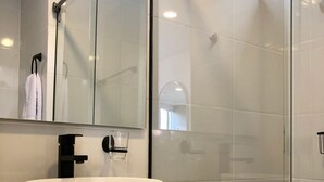 Une salle de bain moderne avec un grand lavabo sur pied blanc, un robinet noir et une cabine de douche en verre.