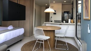 Une chambre d’hôtel compacte comprenant un lit, une table à manger avec deux chaises, un coin cuisine et une grande fenêtre.